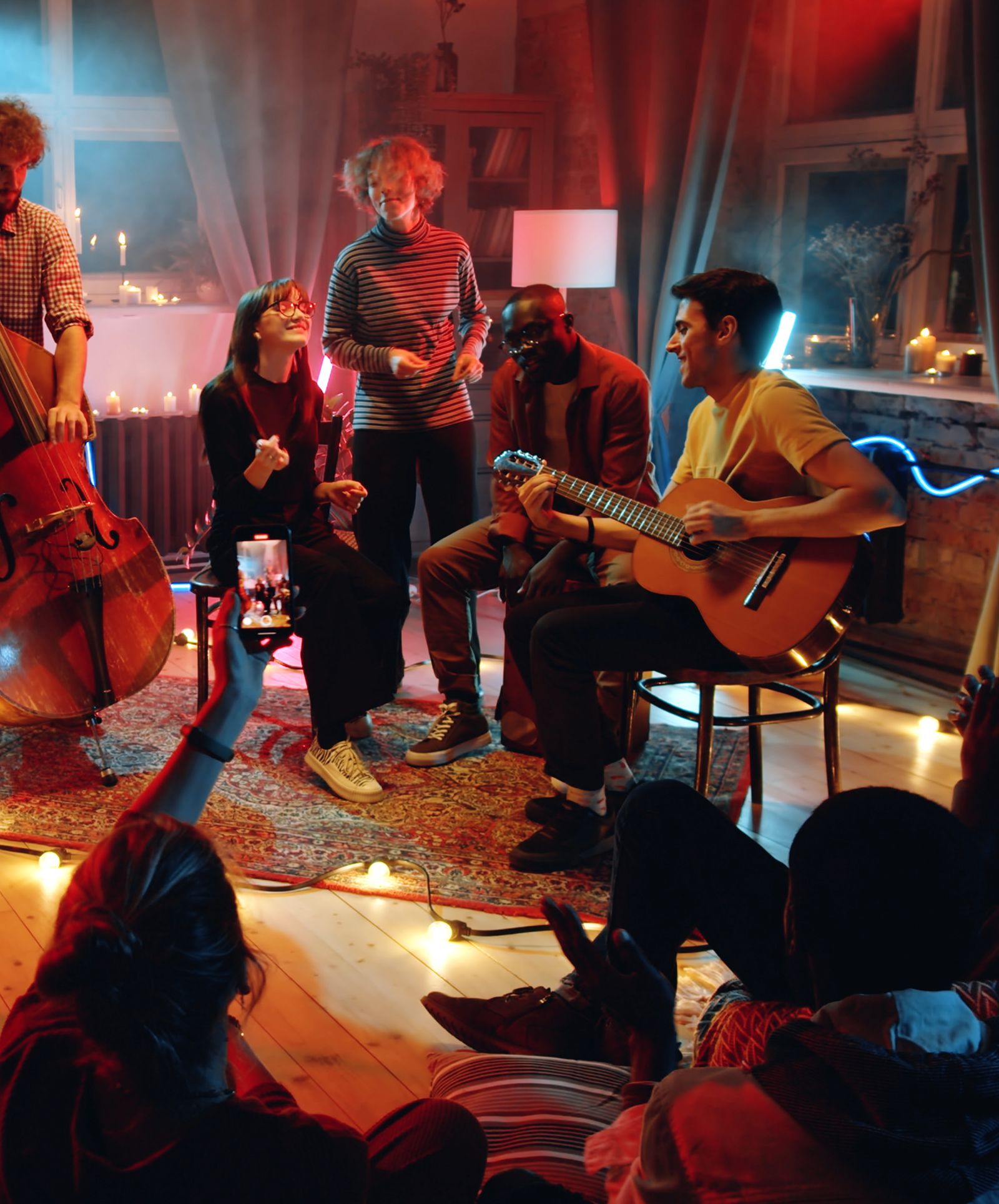 Concierto íntimo en una sala: músicos con guitarra y contrabajo tocan rodeados de amigos